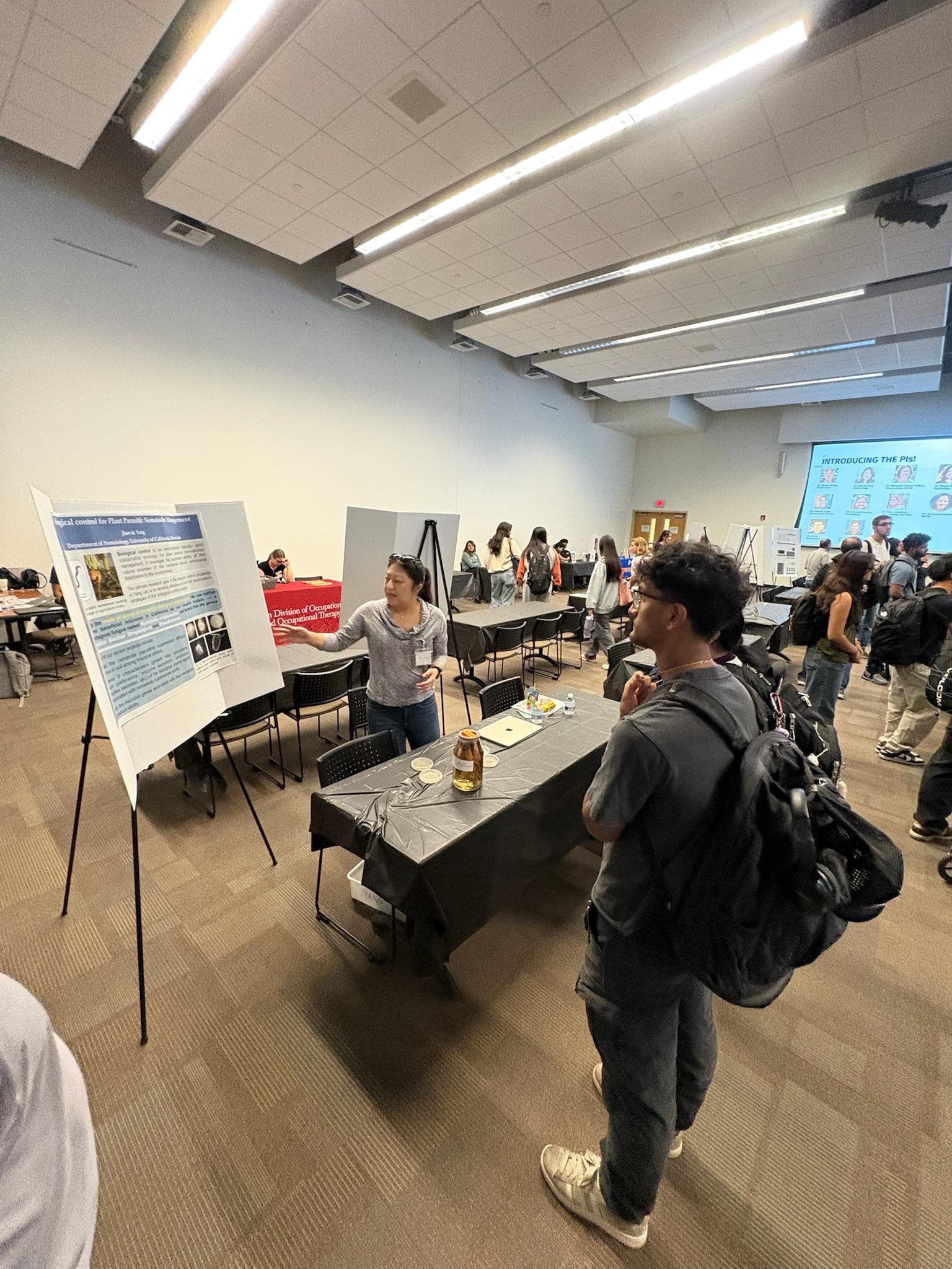 A student speaking with a researcher beside a scientific poster at the Undergraduate Research Mixer